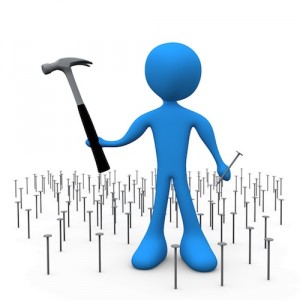 Overwhelmed Blue Person Holding A Hammer And Nail While Standing In A Patch Of Many Nails Clipart Illustration Image